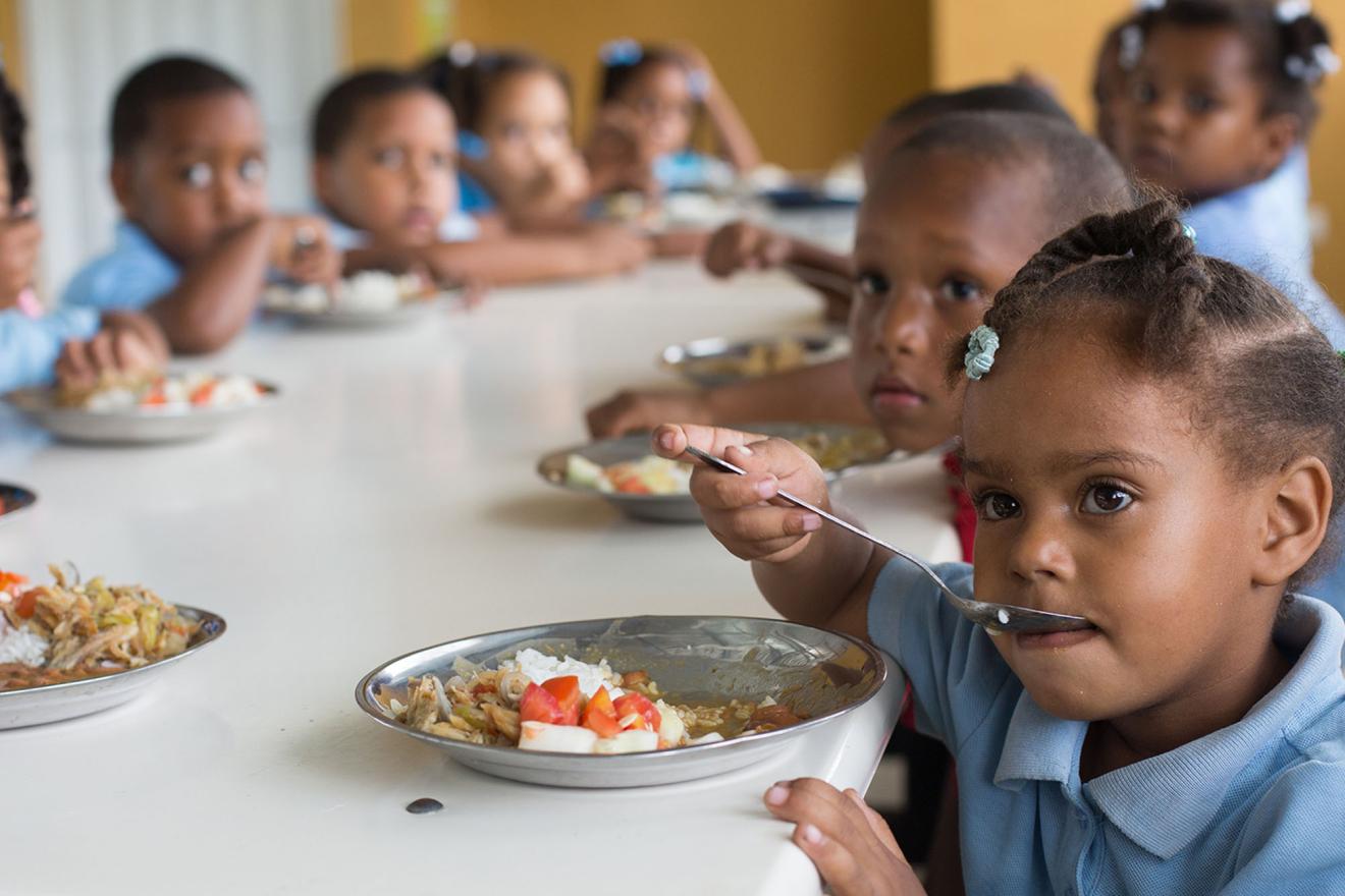 Un grupo de niños sentados alrededor de una mesa y comiendo en una escuela de El Salvador.