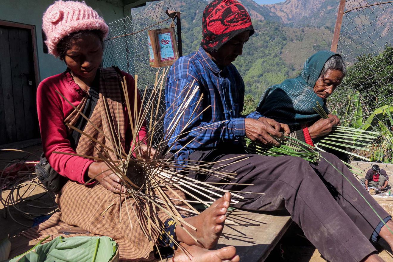 Three people are sitting on the floor, working with bamboo leaves.