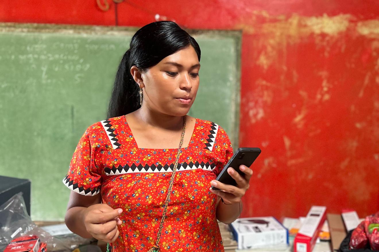 Une jeune femme autochtone, habillée de rouge, regarde son téléphone