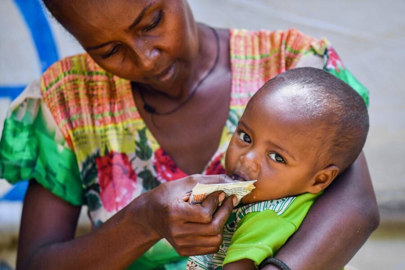 A mother feeding her child a special peanut paste from a sachet.