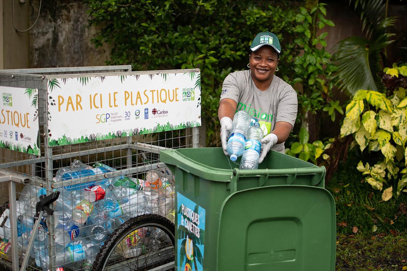 A woman placing plastic bottles into a green recycling bin.