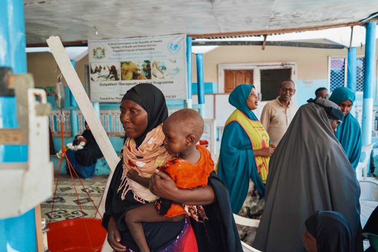 A woman carrying a child among other people in a health center.