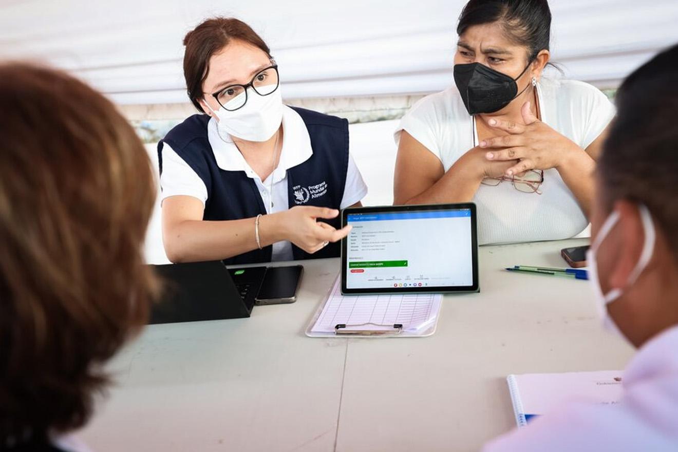 Unas mujeres muestran una tablet con información a unas beneficiarias del plan