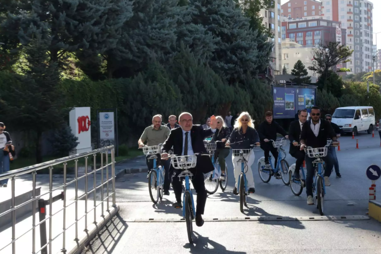 People cycling on campus road with trees and buildings in the background.
