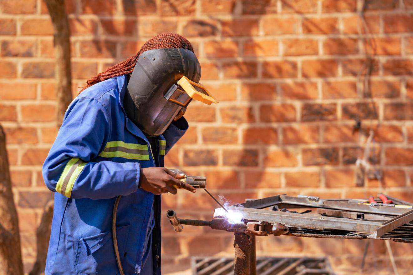 Une jeune femme soude un cadre de fenêtre dans une cour ouverte