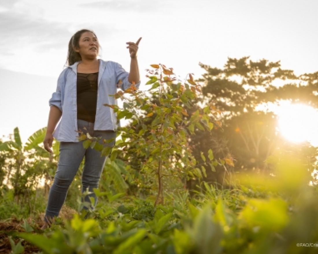 A woman working in the field points at something out of frame 