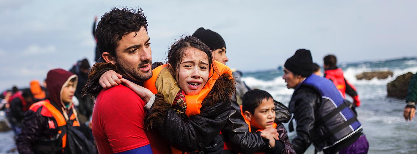 Primer plano: un trabajador de ayuda humanitaria transporta a una niña, rescatada de un barco de refugiados. 