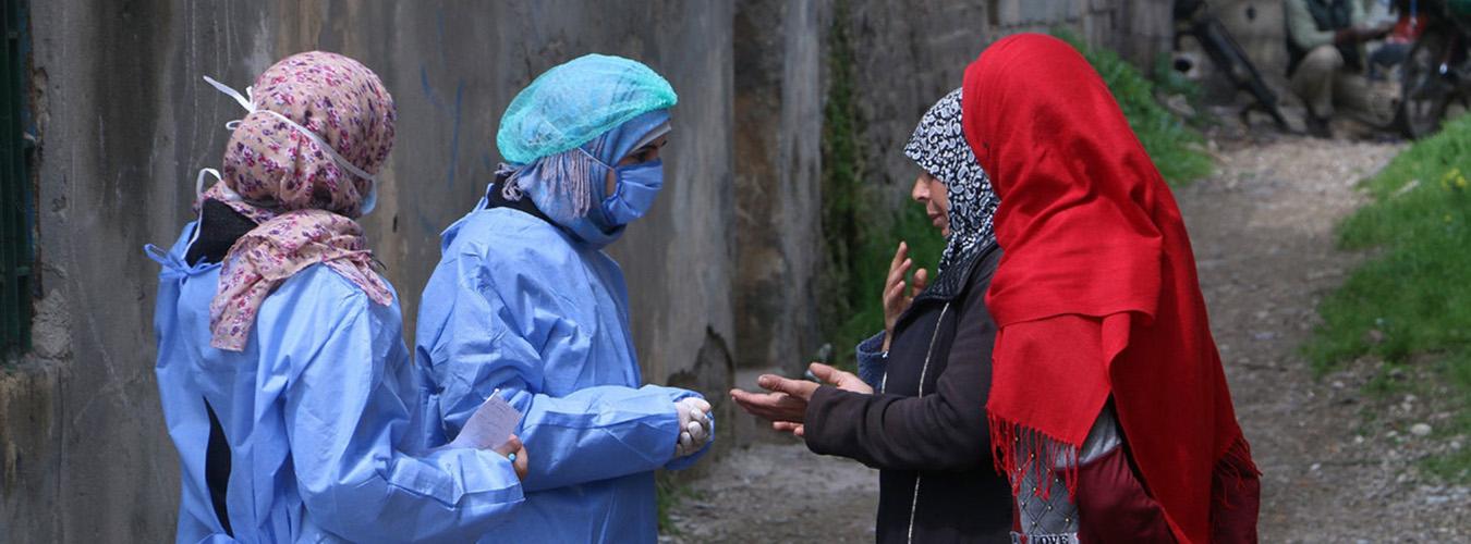 Dos mujeres con equipos de protección hablan con otras dos sin máscaras.