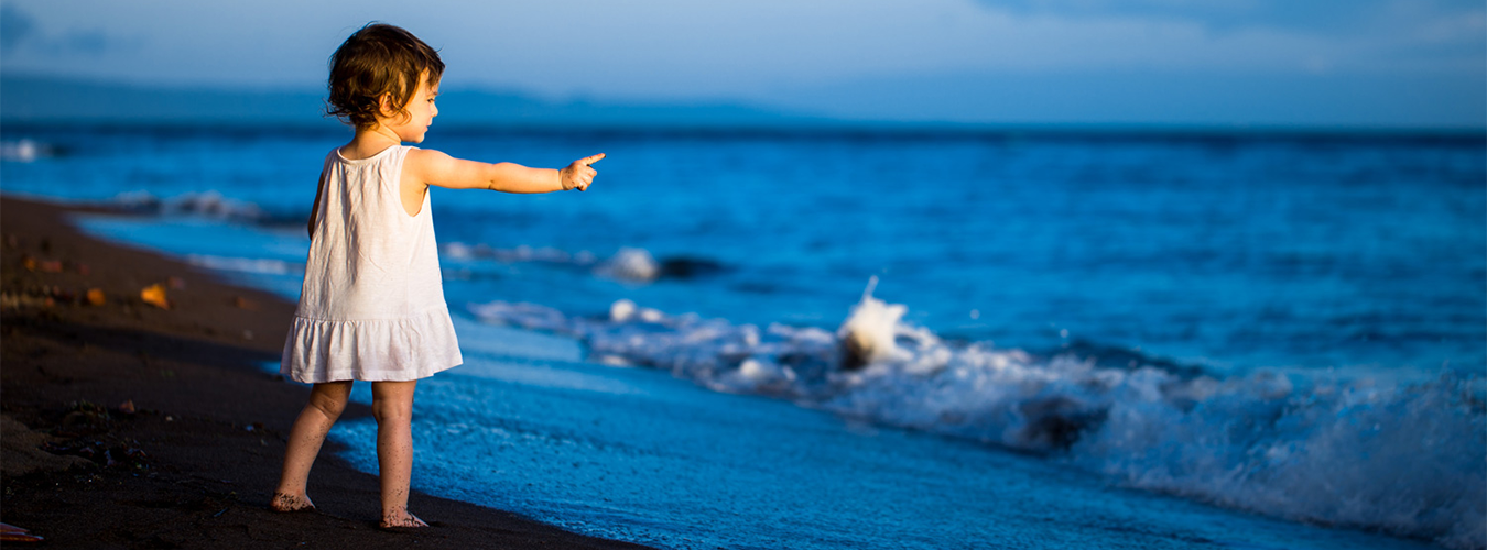 A girl in the shore pointing towards the sea.