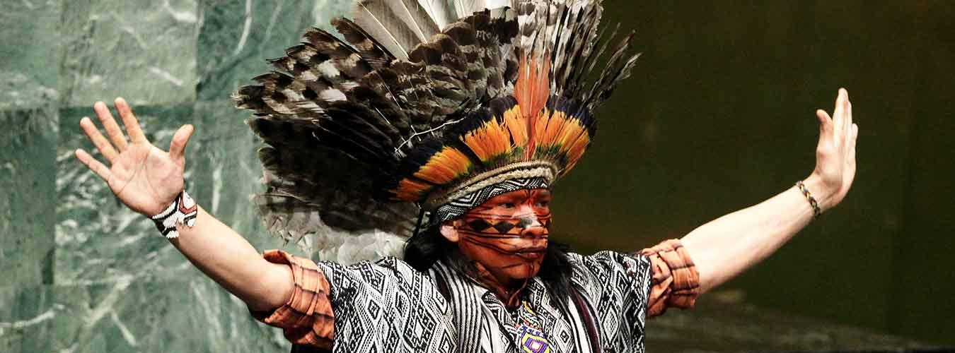 An indigenous leader from the Western Amazon in Brazil, dressed in impressive traditional attire, delivers an invocation at the General Assembly hall in New York.