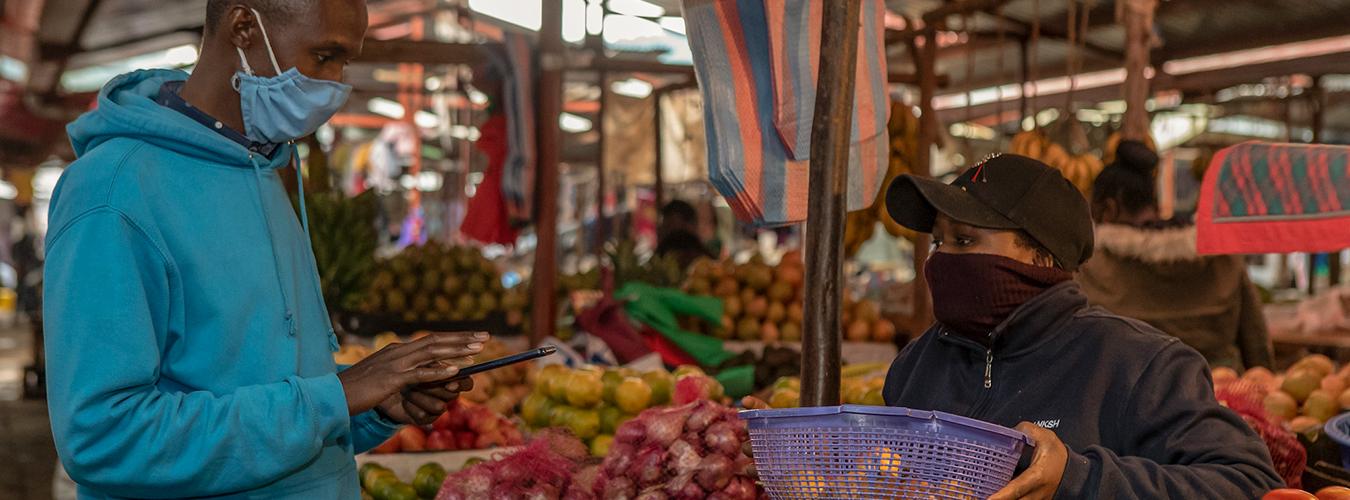 Transaction entre une vendeuse et un consommateur dans un supermarché ; tous les deux ont le visage couvert comme mesure de prévention contre la COVID-19.