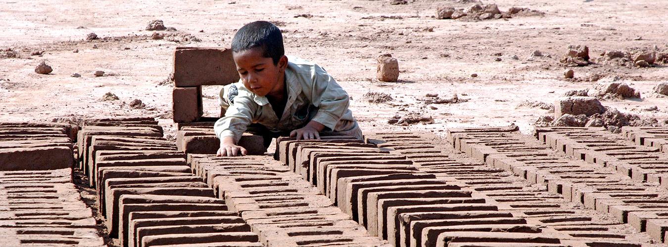 Un niño pequeño se apoya en una hilera de ladrillos puestos a secar.
