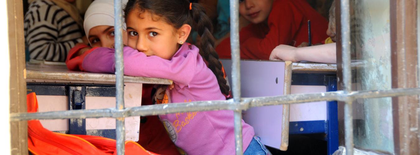 A girl looks out a window with bars from inside the classroom.