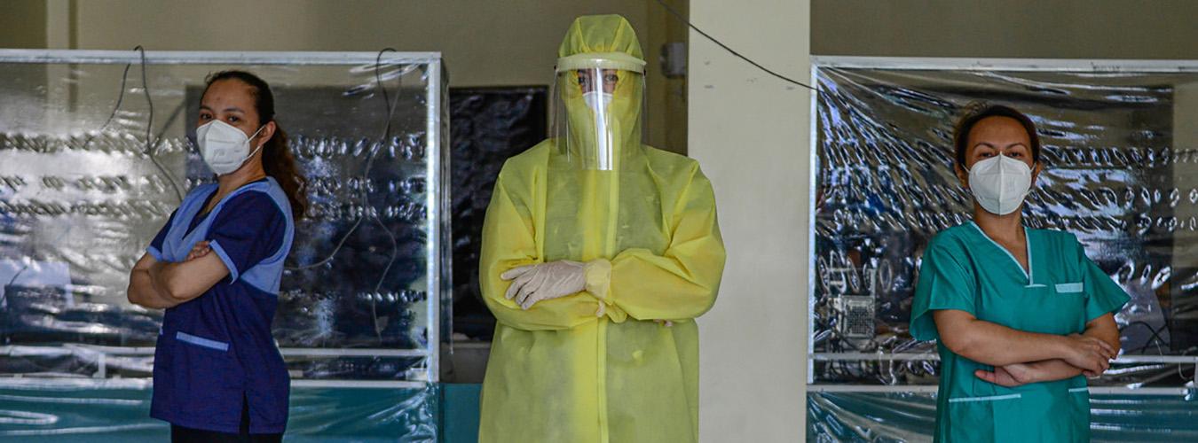 Trois femmes du domaine sanitaire sont vêtues de tenues de protection. 