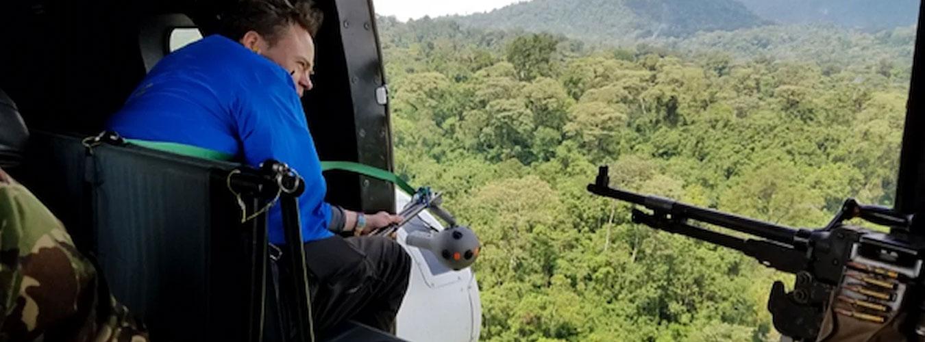 Une homme filme depuis un hélicoptère survolant une forêt.