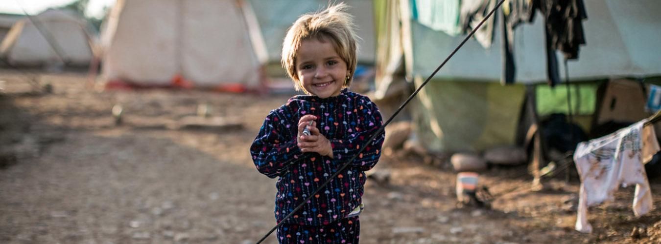 Маленькая девочка стоит возле палаток в лагере беженцев в Ираке.