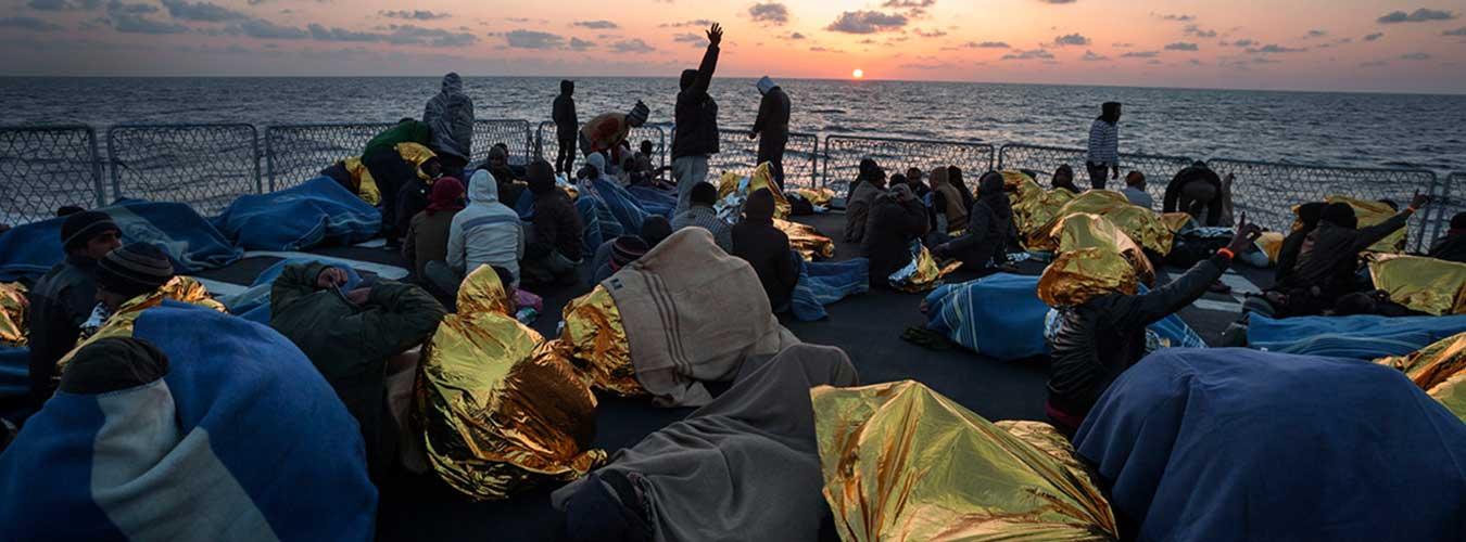 Un groupe de personnes secourues sur le pont d'un navire de la marine italienne au coucher du soleil en Méditerranée. 