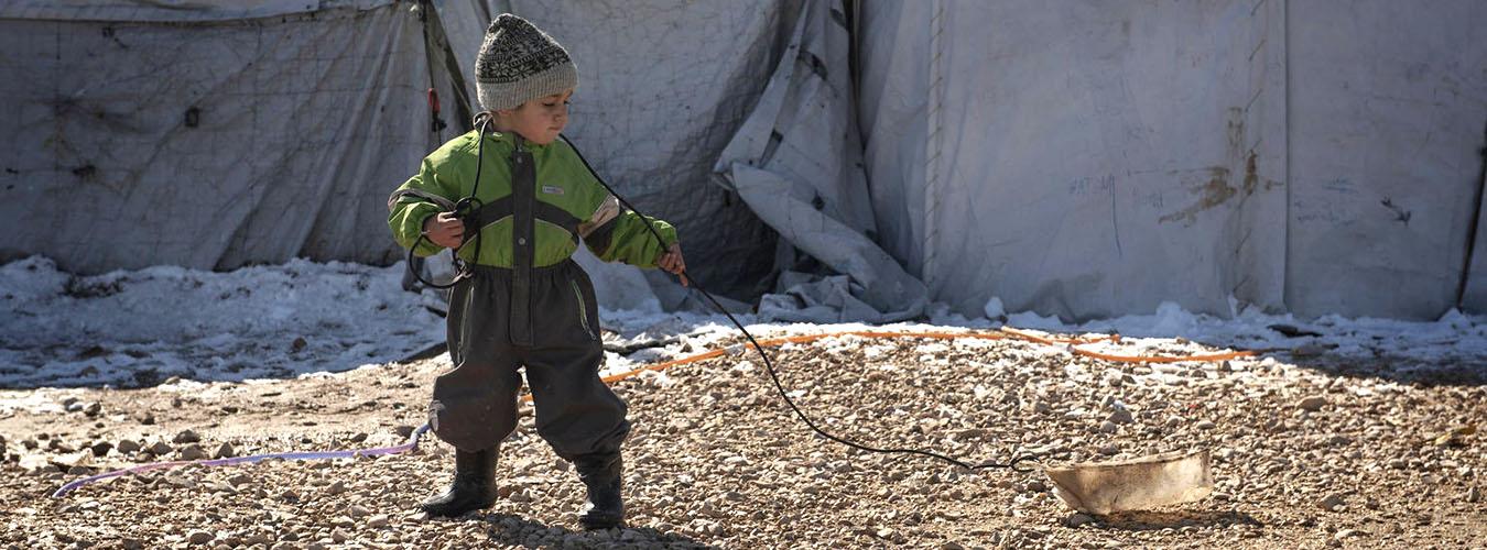 Un enfant traîne un récipient en plastique vide avec l'aide d'une ficelle.