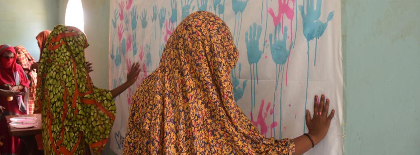 Women leave their hand prints in pink and light blue on a poster.