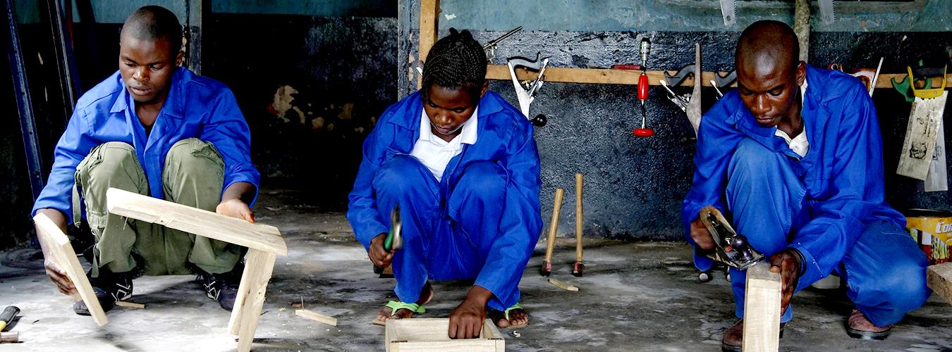 Dos hombres y una mujer vestidos con monos de trabajo azul trabajando con madera. 