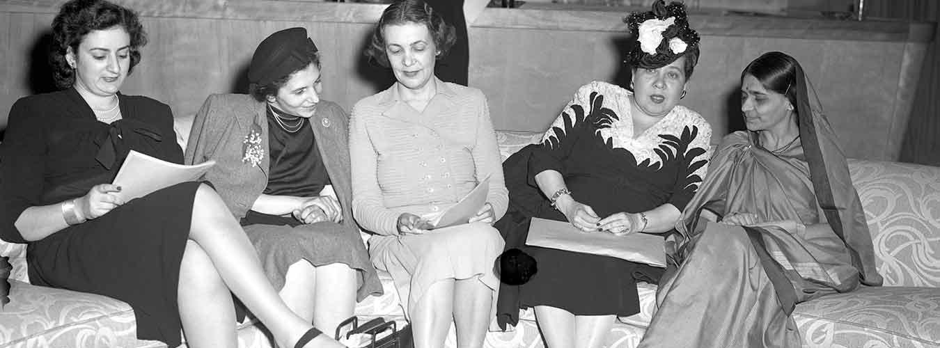 Archival black and white photo of the ladies from the Sub-commission on the Status of Women sitting on a couch, discussing the documents at hand.