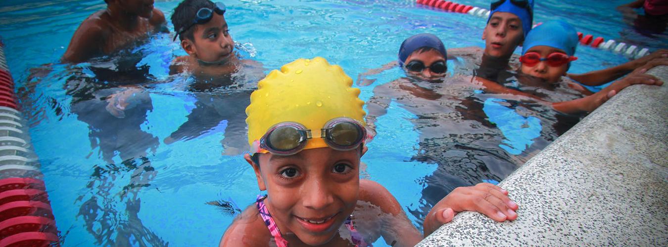 Niños con gafas y gorros nadando en una piscina.
