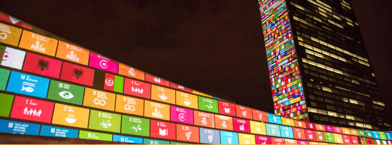 أيقونات أهداف التنمية المستدامة وأعلام الدول الأعضاء مسقطة ضوئيا على مقر الأمانة العامة للأمم المتحدة في نيويورك.