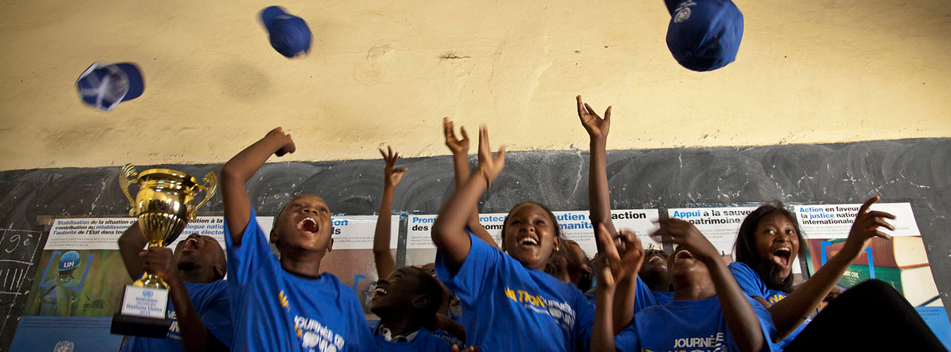 Children happily throw their caps in the air in a classroom. 