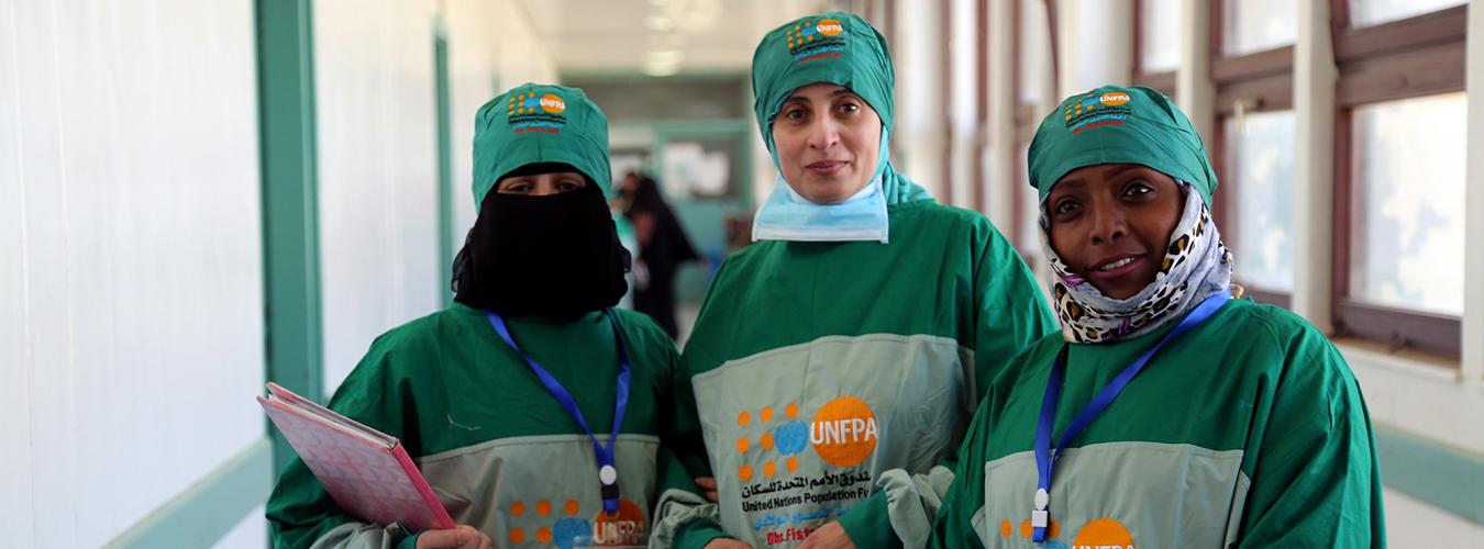 Tres sanitarias con ropas médicas que muestran el logotipo de la agencia de la ONU, UNPFA