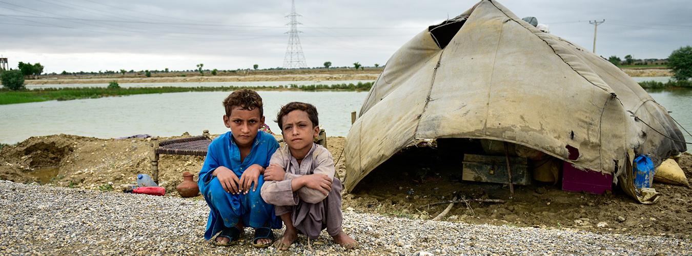 two boys sit beside a tent next to a flooded area