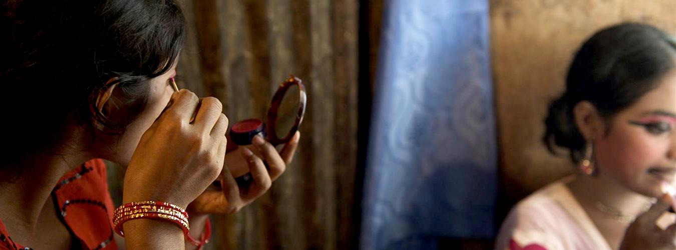 Une jeune femme se maquille devant un miroir. 