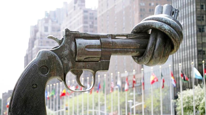 A sculpture of a large scale gun with its nozzle knotted on display at UNHQ with Member States' flags fluttering in the background.