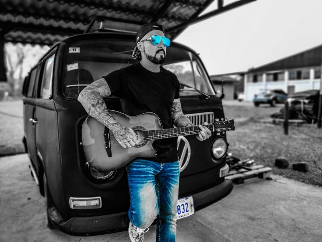 Un hombre se apoya en una minivan mientras toca la guitarra.