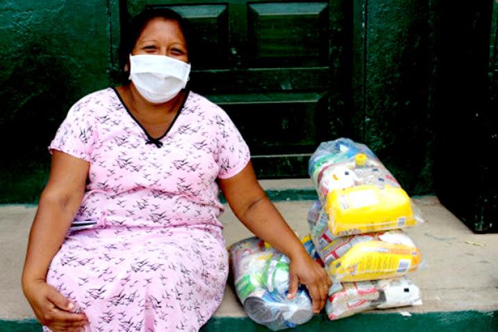 Woman receiving food from WFP for their children in Riohacha, La Guajira, Colombia. Masked woman sits next to four bags of rations.
