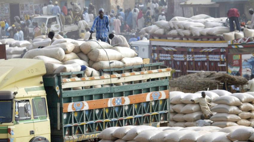 A busy outdoors scene shows trucks laden with sacks of food.