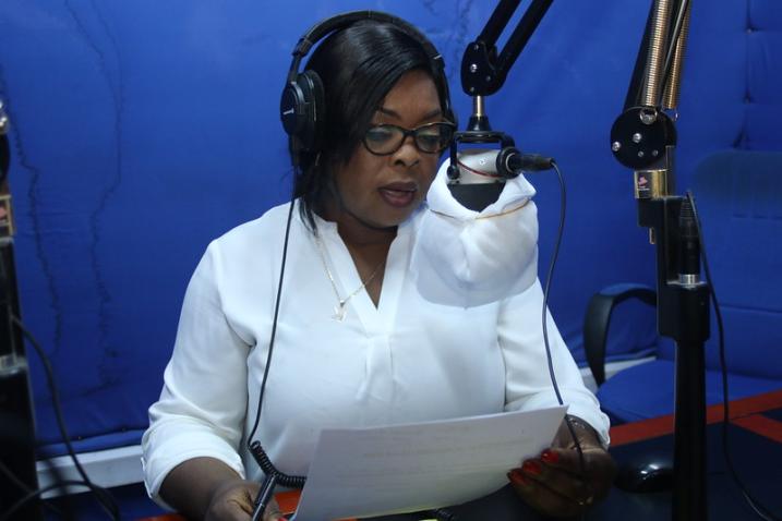 A woman is seen inside a studio speaking into a microphone that is wrapped with white cloth.