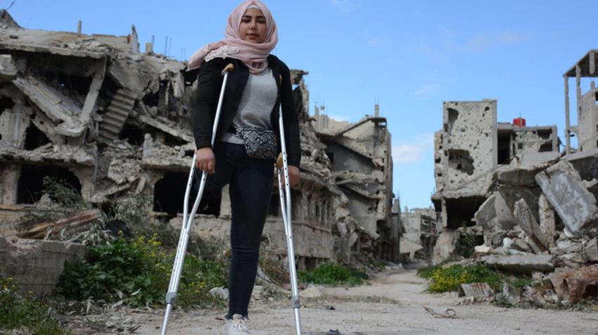 Girl with crutches in front of bombed buildings