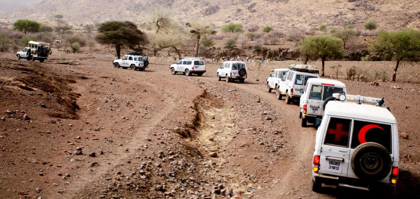 Red cross and UN and various other vehicles drive through a rough terrain.