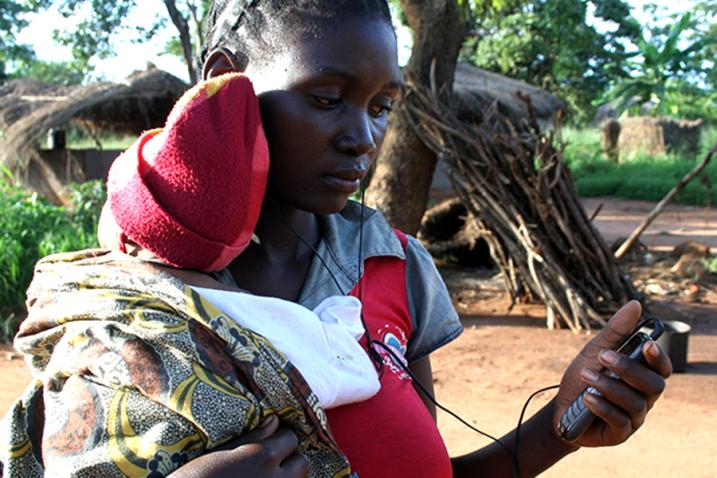 A woman carrying her baby looks at her mobile screen. 
