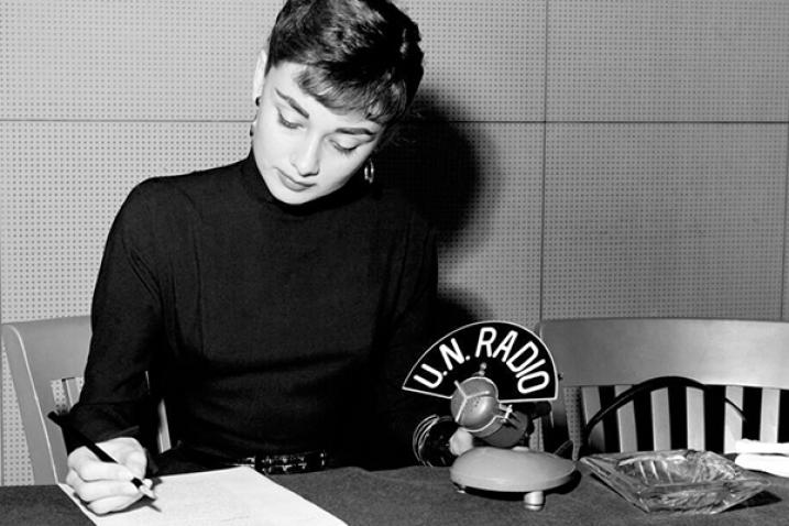 Audrey Hepburn is writing a note inside a radio recording studio at U.N. Headquarters.