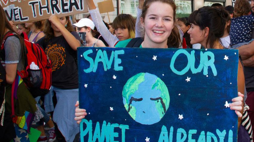 Young girl at a climate march holding a sign with a picture of a crying Earth and the text "Save our planet already."