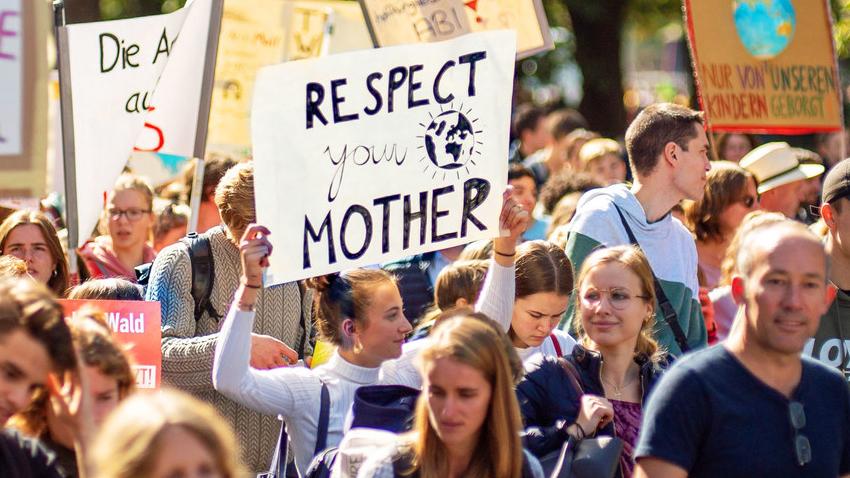 A climate strike where a young person is holding an sign written "protect your mother"