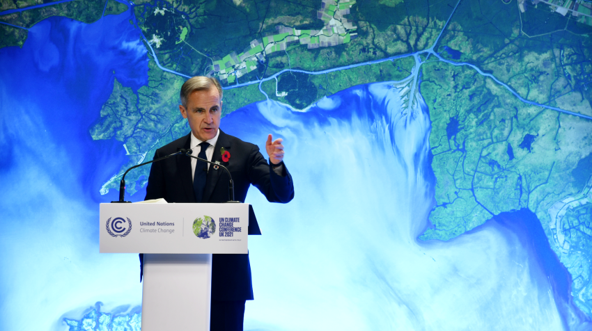 Mark Carney stands in front of a coastline map giving a speech during COP26