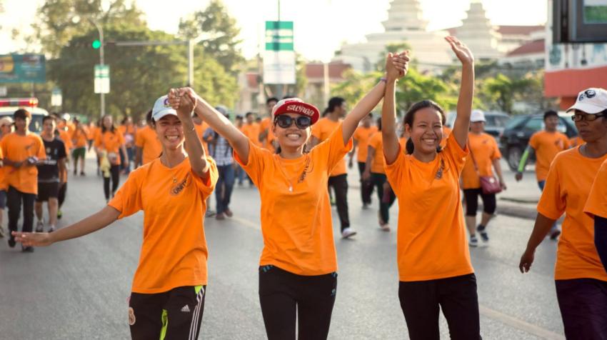 Tres chicas jóvenes vestidas de naranja caminan entre una multitud vestida también de naranja.