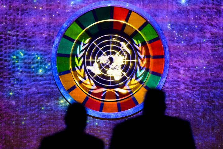 The SDG multicoloured wheel is project around the round gold UN emblem of the map of the world surrounded by olive branches