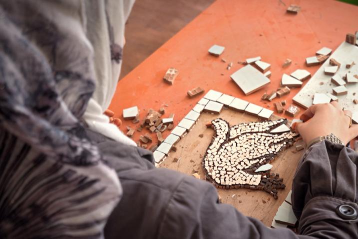 A woman creating a mosaic depicting a dove.
