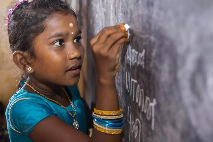 A young girl writing on a blackboard in class.