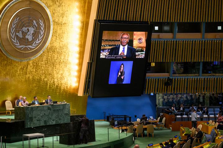 Philemon Yang (on screen) delivers a message in the GA Hall, an sign language interpreter is shown on the screen