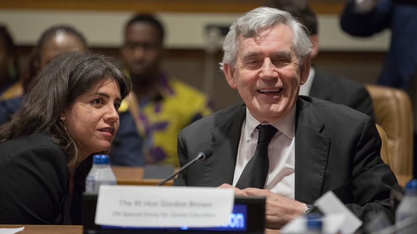 Gordon Brown is seen sitting at a table with his name plate. He is smiling in a relaxed happy mood.