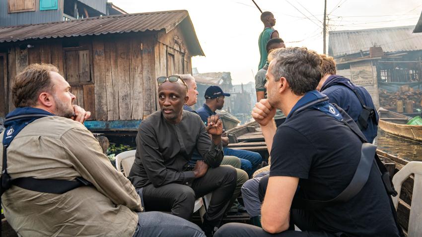  Mohamed Yahya and the Danish Minister for Development, among others, are in a boat touring informal settlements  built on stilts along a lagoon.